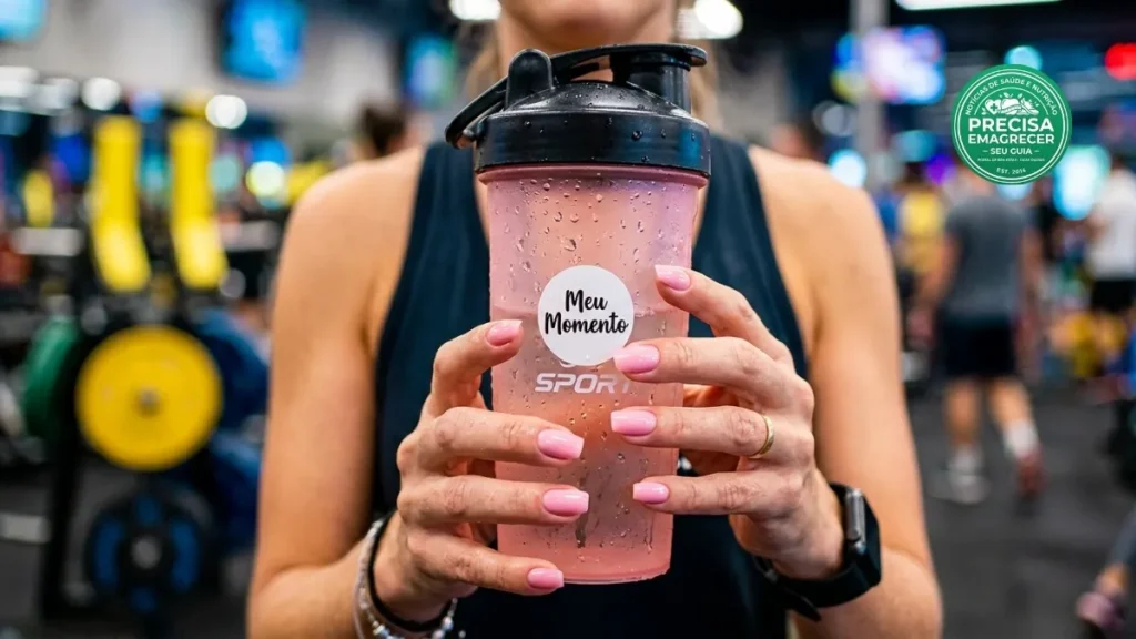 Mãos de mulher segurando um shake rosa refrescante em uma garrafa moderna.